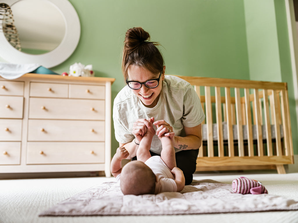 Mother smiling at baby lying on the floor in their nursery room with nursery items