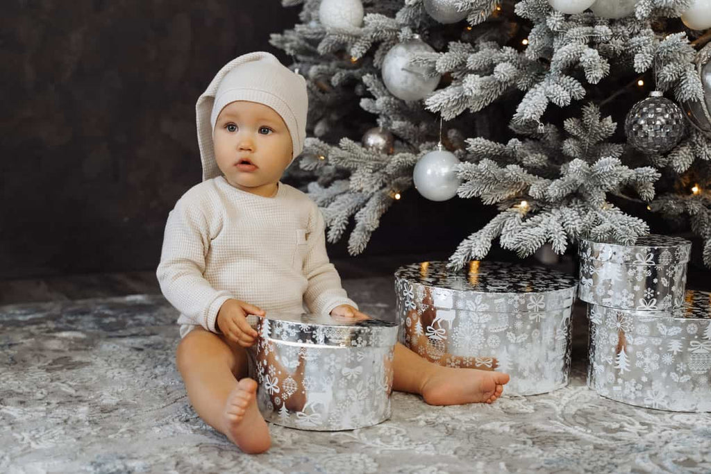 Baby sitting in front of a silver Christmas tree opening presents with purpose