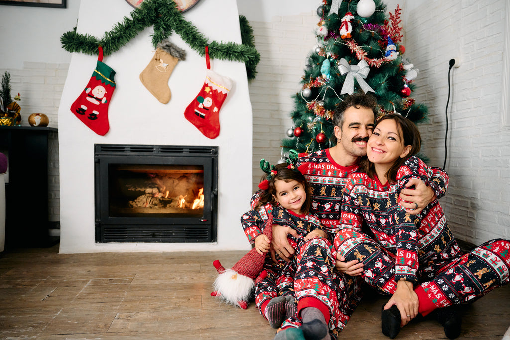 Family in matching Christmas pajamas in front of the fire and Christmas tree with baby items on sale